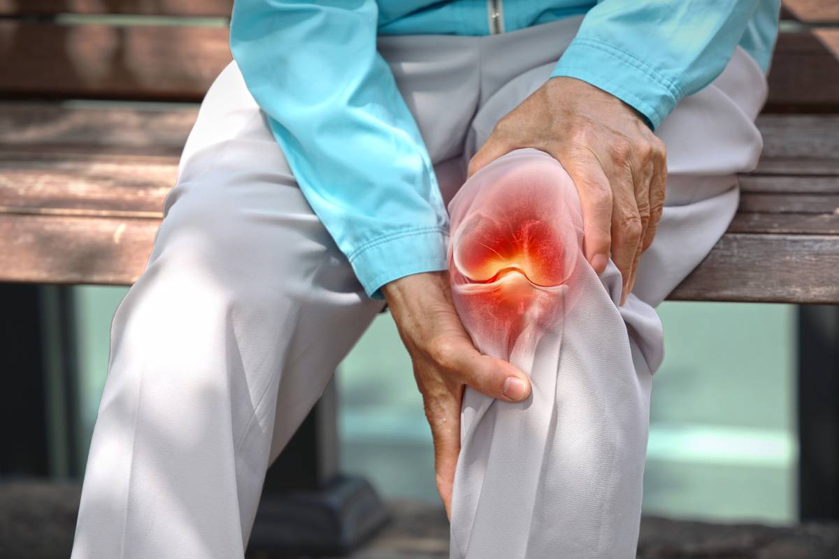 Closeup view of an elderly man sitting on a bench holding his knee in pain and a hologram of knee joint shown in red.