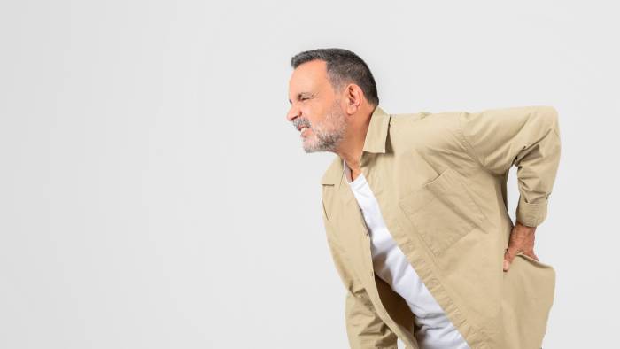 Side view of a senior man leaning forward holding the left side of his hip in pain.